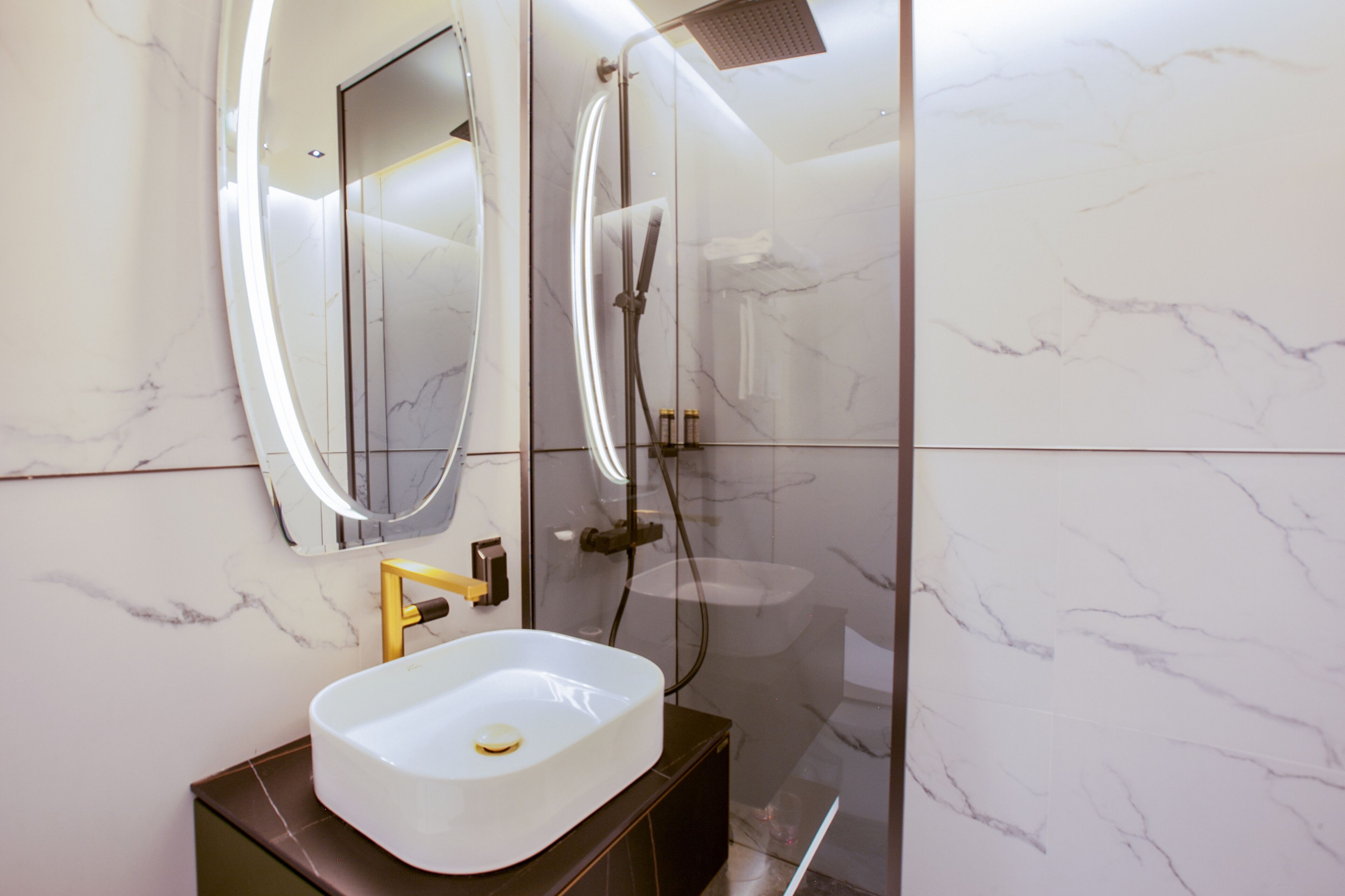 A modern bathroom with a marble wall, a white sink, and a glass-enclosed shower.