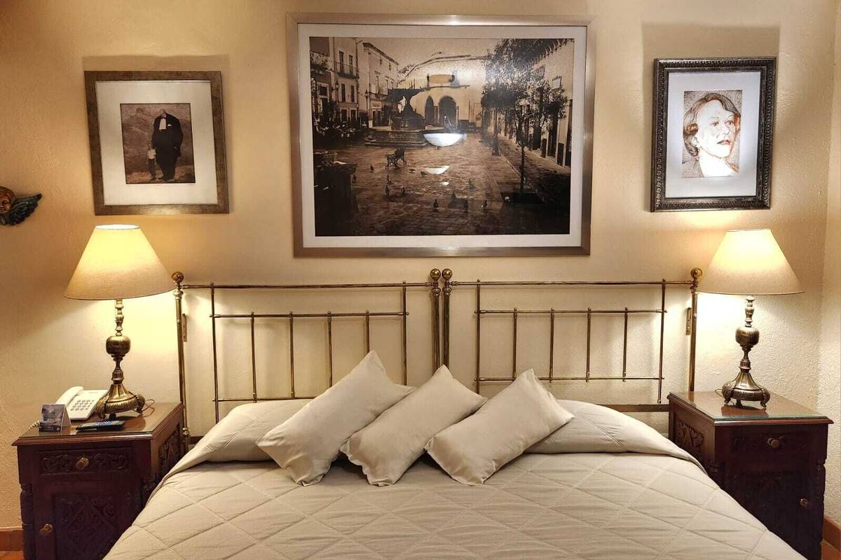 Un lit recouvert d’une courtepointe, deux tables de chevet avec des lampes et trois tableaux encadrés accrochés au mur.