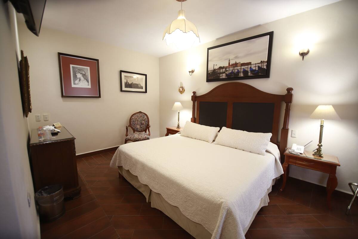 Une chambre à coucher bien aménagée, avec un grand lit, des tables de chevet, une chaise et un téléviseur fixé au mur.