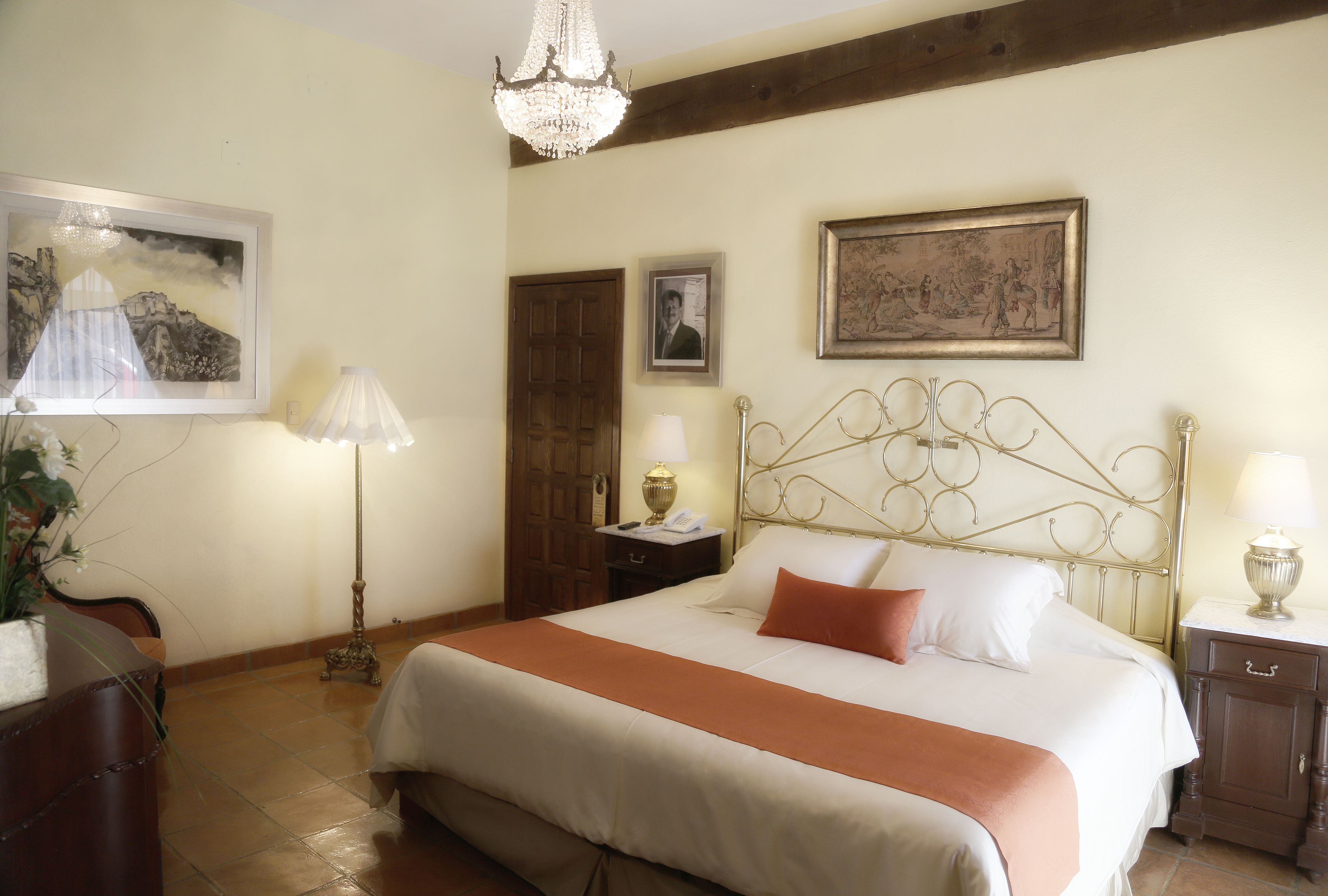 A neatly made bed with a headboard, two bedside tables with lamps, a wooden door, and a framed picture on the wall.