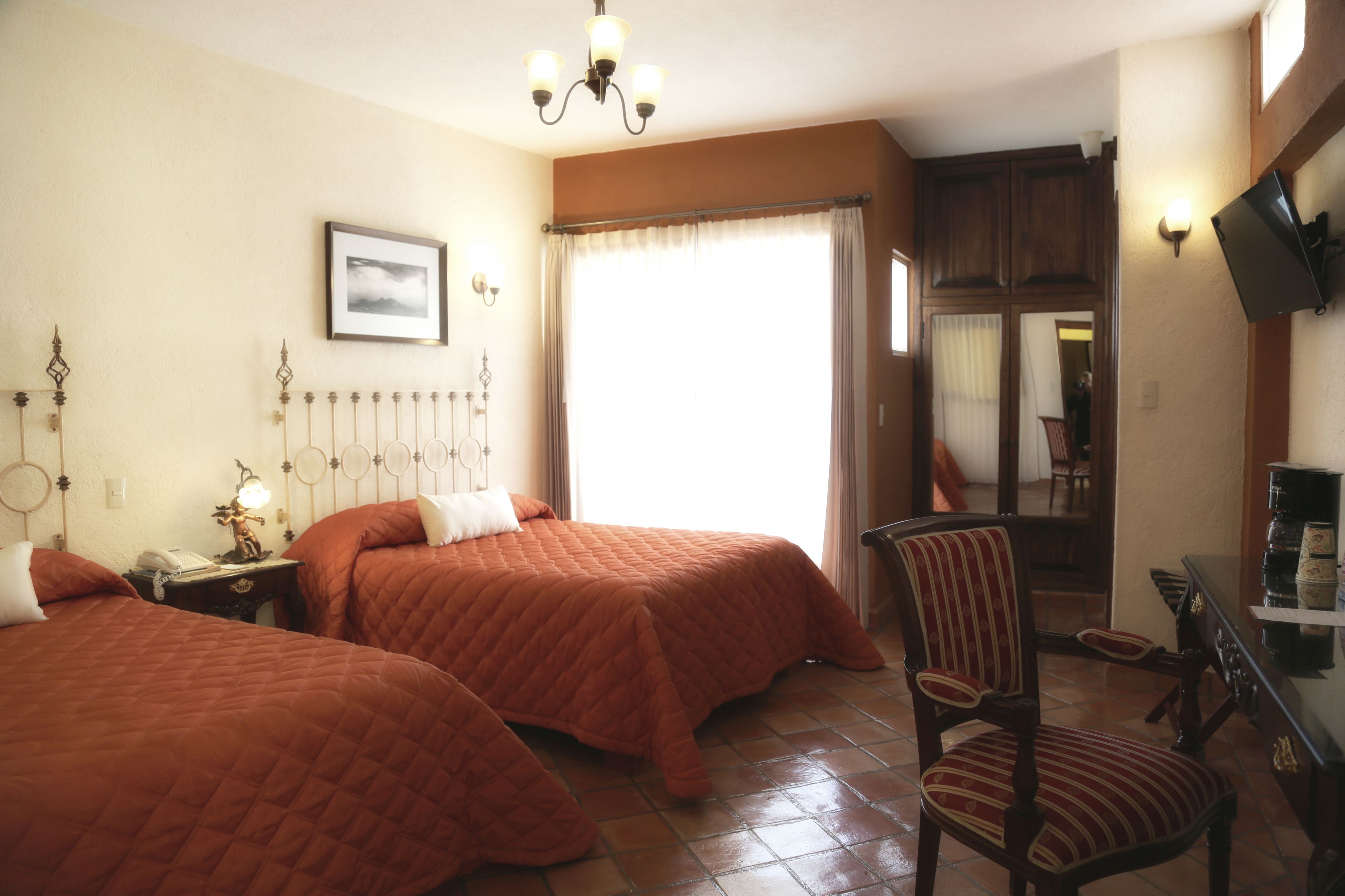 Habitación de hotel con dos camas, una silla, un escritorio con cafetera y un televisor.