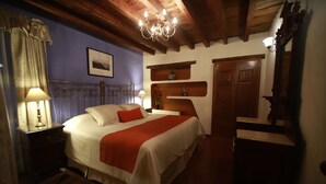 Un dormitorio con cama, mesitas de noche, cómoda, candelabro y vigas de madera en el techo.