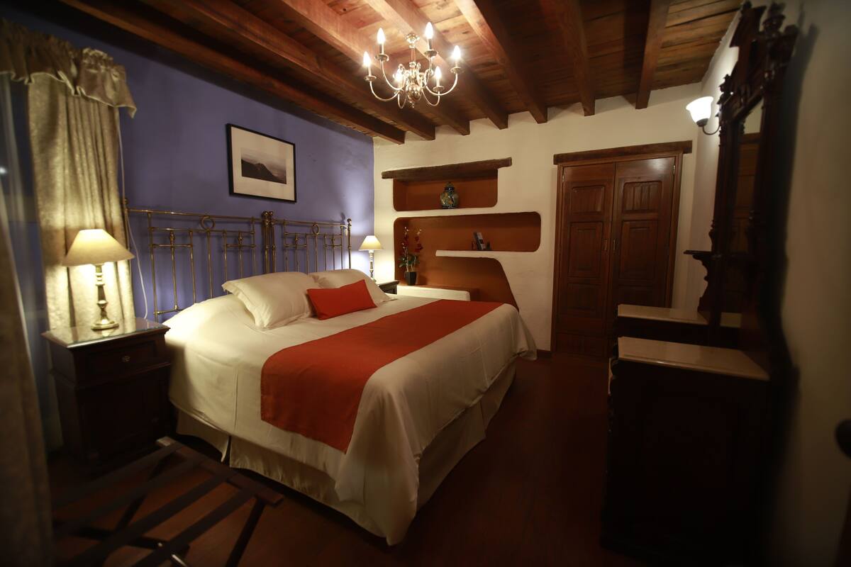 Une chambre à coucher avec un lit, des tables de chevet, une commode, un lustre et des poutres en bois au plafond.
