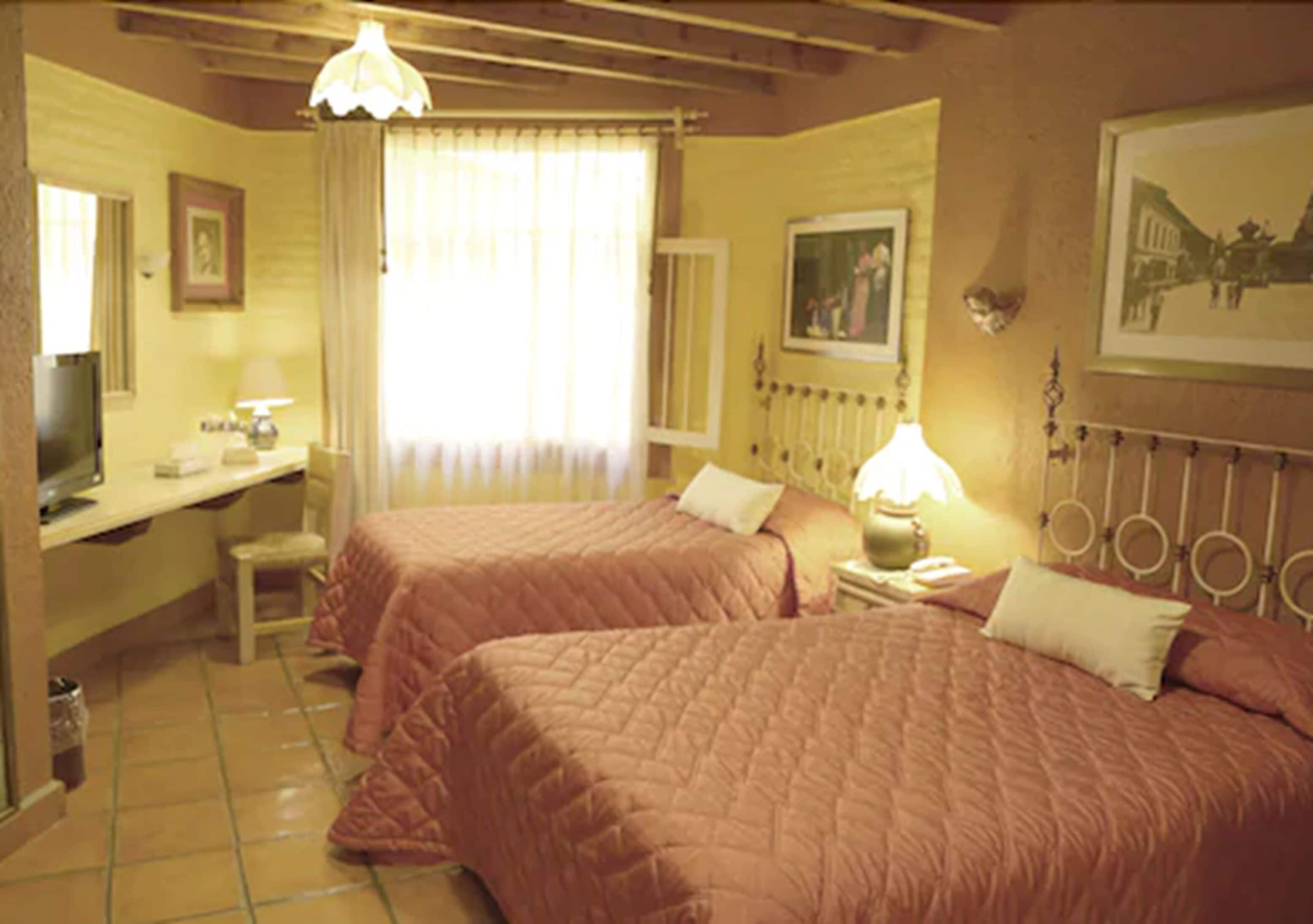 A room with two beds, a desk, a chair, and a television.