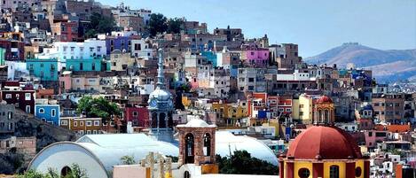 Un paisaje urbano en una ladera pronunciada, con edificios de colores, una imponente torre del reloj y una gran estructura en forma de cúpula.