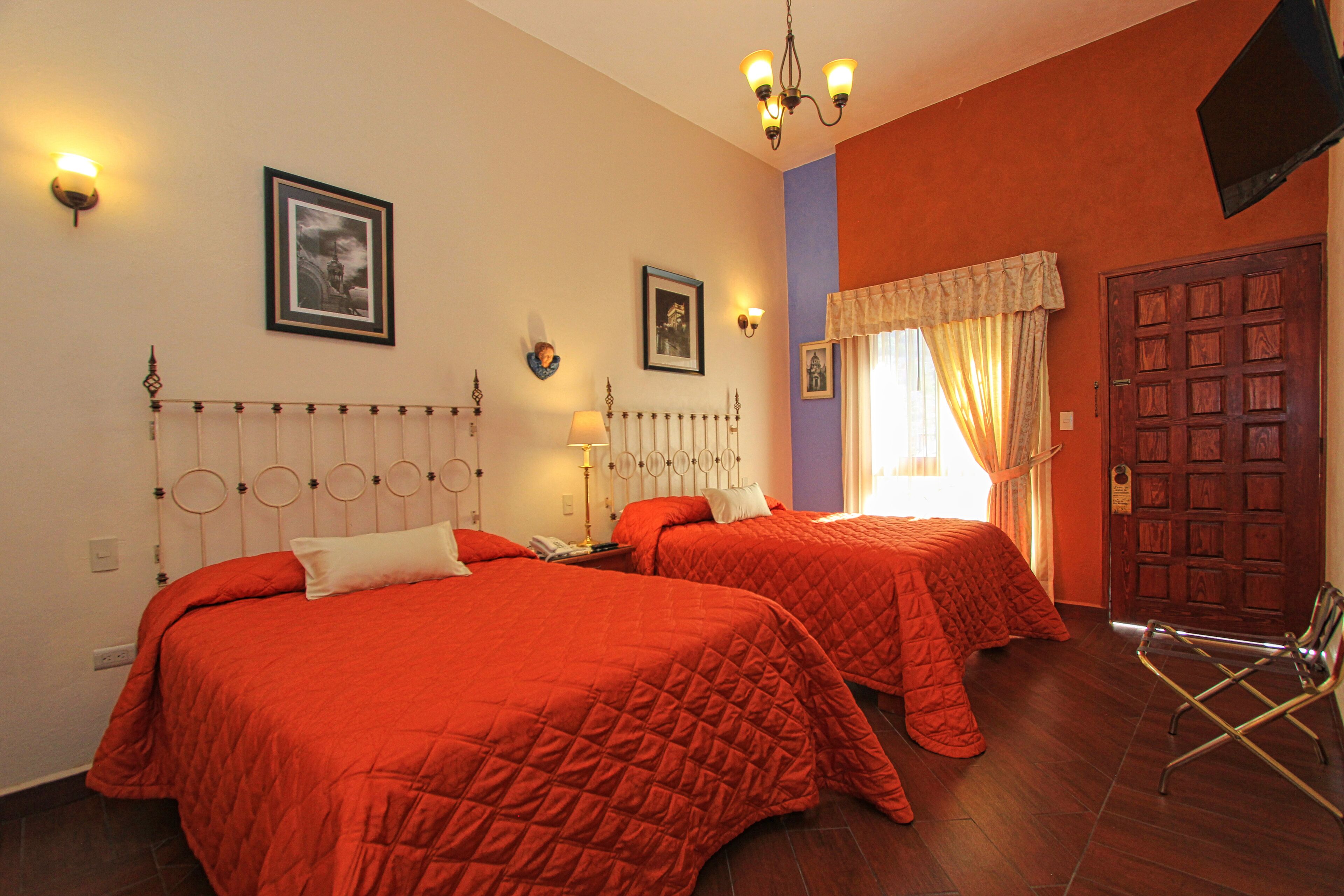 Une chambre d’hôtel avec deux lits, un lustre, une télévision et une porte.