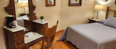 A bedroom with a bed, a wooden chair, a desk with a coffee maker, and two wall-mounted lamps.