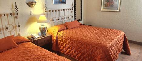 Une chambre d’hôtel avec deux lits, une table de chevet avec une lampe, un miroir et deux tableaux encadrés au mur.