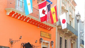 Un edificio con balcones, un letrero que dice "Meson de los Poetas" y varias banderas, incluyendo las de Canadá y Japón.
