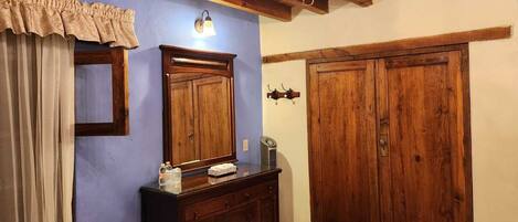Una habitación con techo de madera, un candelabro, un amplio armario de madera, un aparador con objetos encima y una lámpara fijada a la pared.