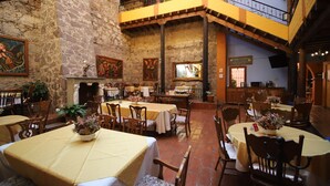 Un restaurante con varias mesas y sillas, una pared de piedra y una escalera que sube a un nivel superior.