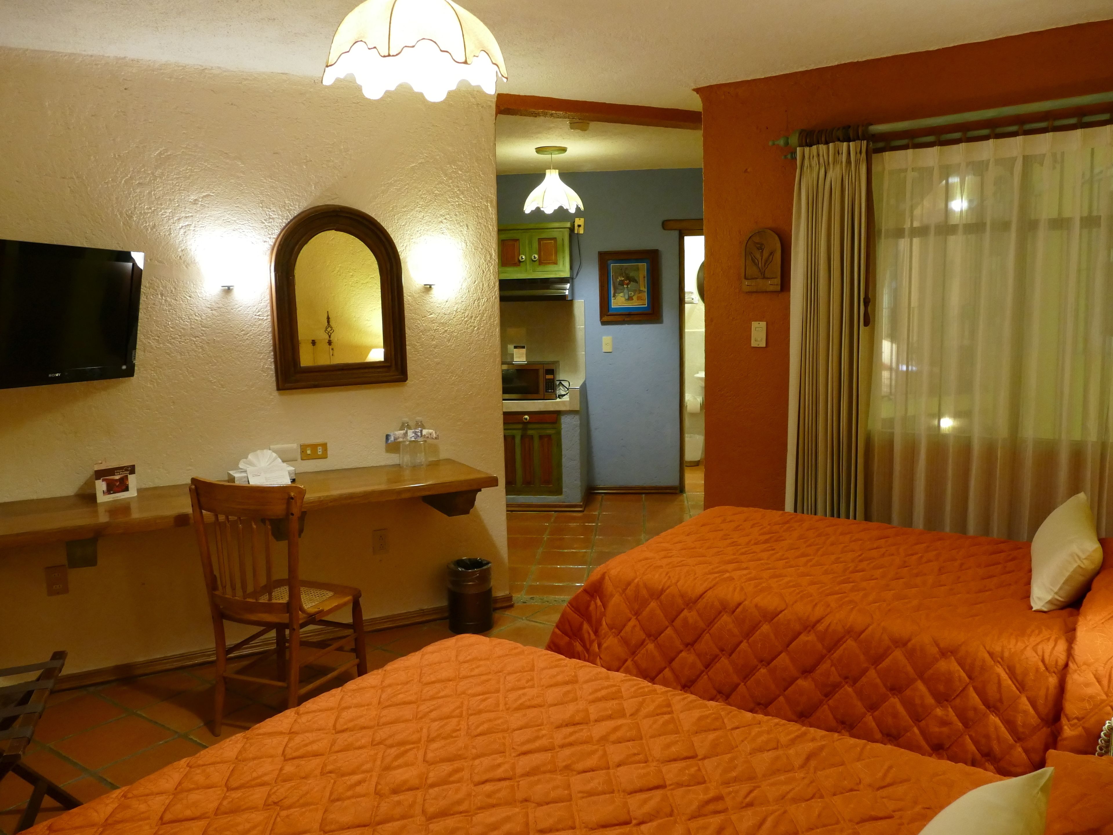 Une chambre d’hôtel avec deux lits, un bureau avec une chaise, une télévision et une salle de bain visible à travers une porte ouverte.