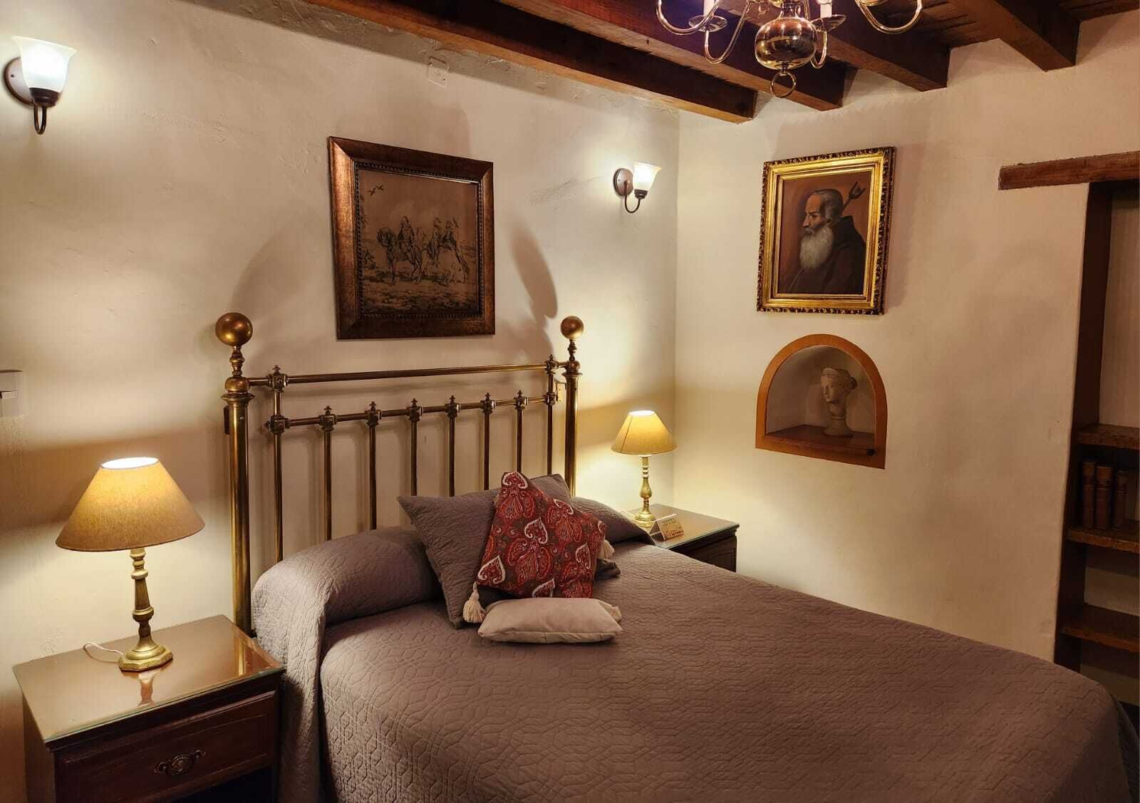 Un dormitorio con una cama, dos mesitas de noche con lámparas, un cabecero de madera y una obra de arte colgada en la pared.