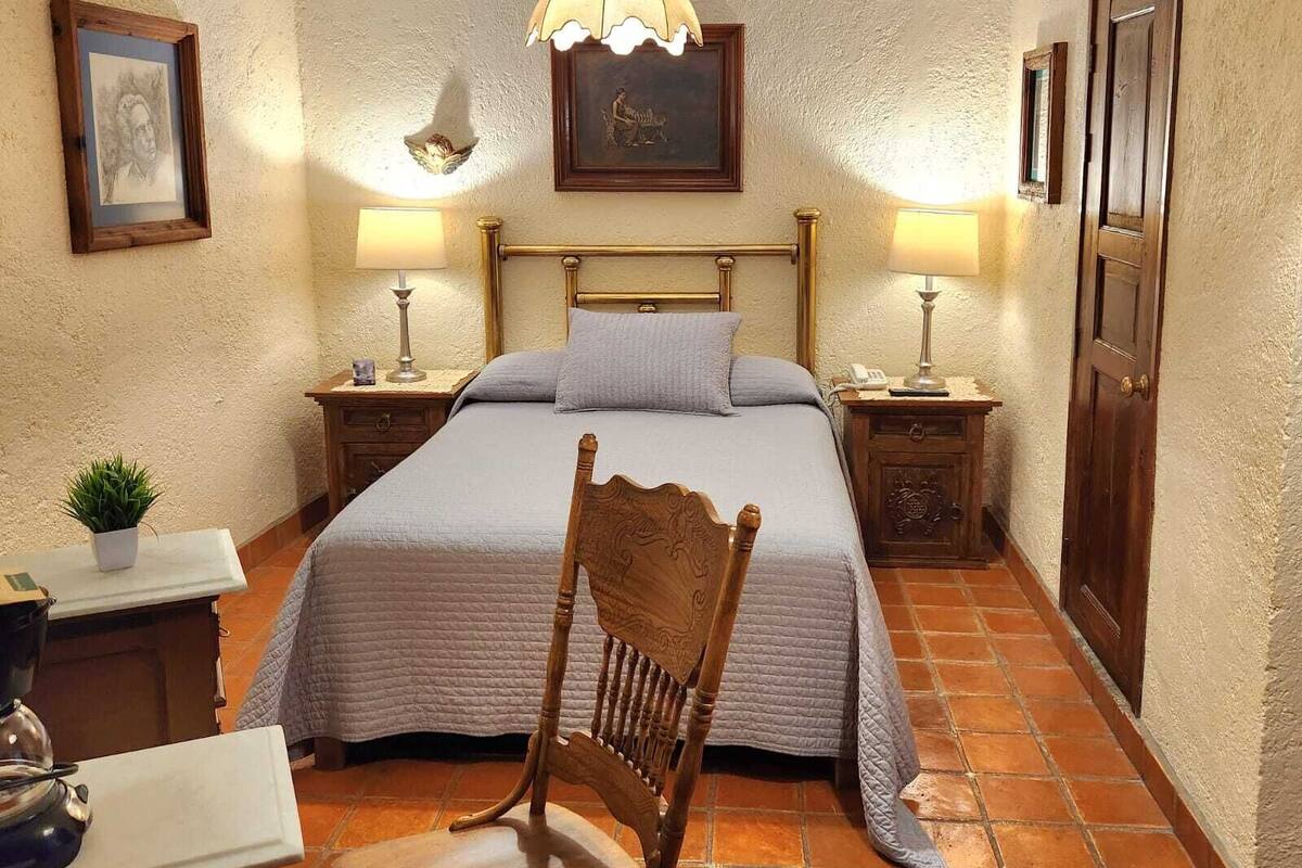 Une chambre à coucher comprenant un lit, deux tables de chevet, une chaise, un bureau, une lampe et une porte.