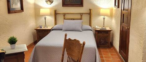 A bedroom with a bed, two bedside tables, a chair, a desk, a lamp, and a door.