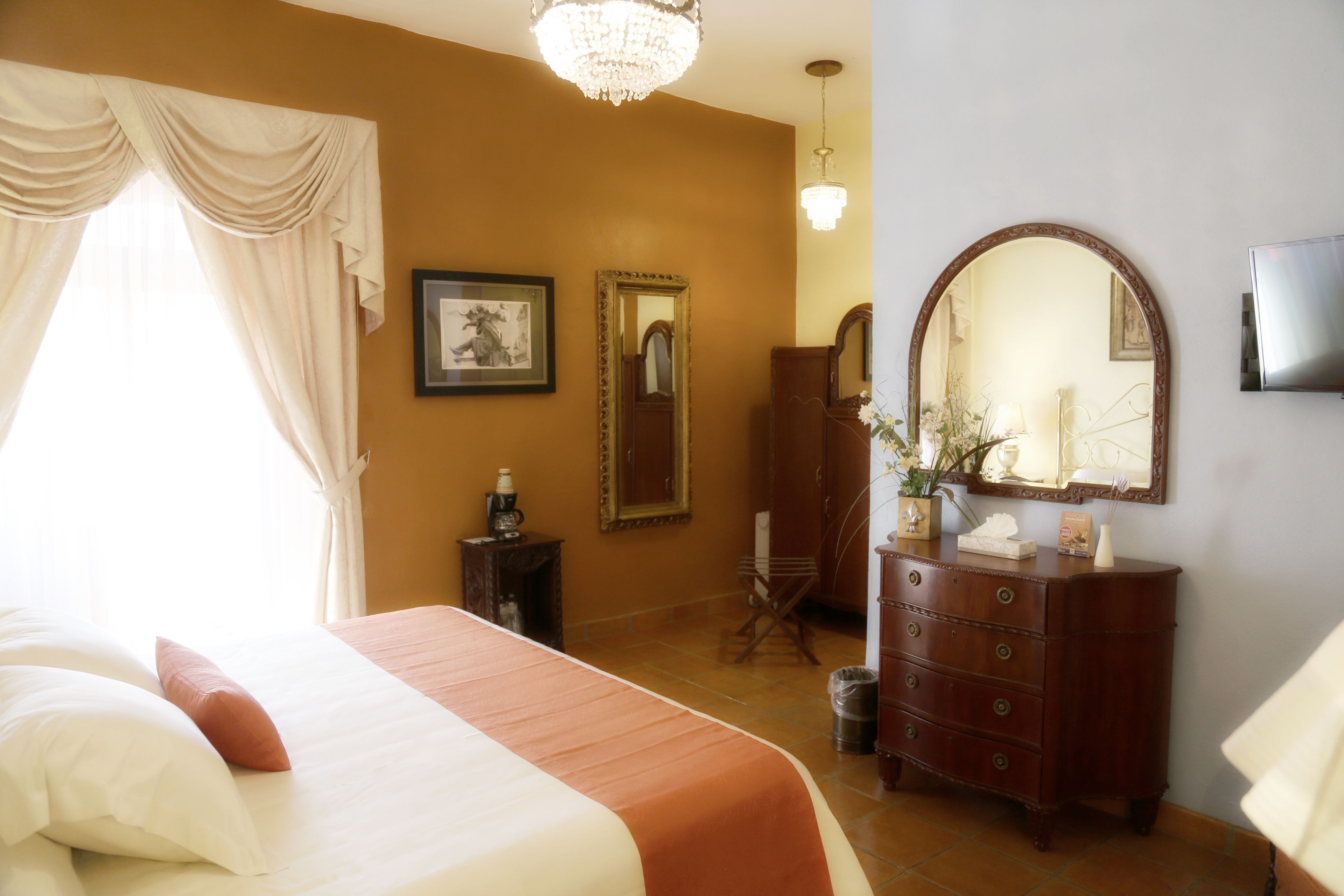 A bedroom with a bed, a dresser, a mirror, and a chandelier.