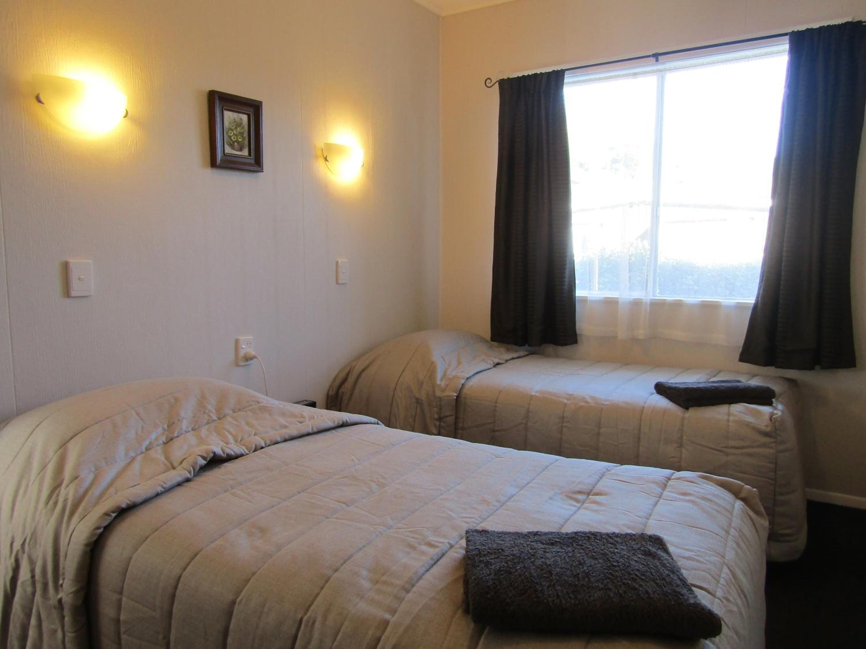 A room with two beds, a window with curtains, and wall-mounted lights.