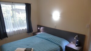 Una habitación de hotel con cama, mesita de noche, lámpara y ventana con cortinas.