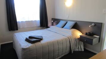 A neatly made bed with a quilt, a bedside table with a lamp, and a nightstand with a camera.