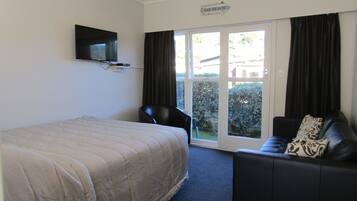 A hotel room with a bed, a TV mounted on the wall, a sofa, and a sliding glass door leading to a balcony.