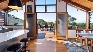 A modern kitchen with a large window, wooden deck, and outdoor seating area. - The Oasis Apartments and Treetop Houses (Byron Bay)