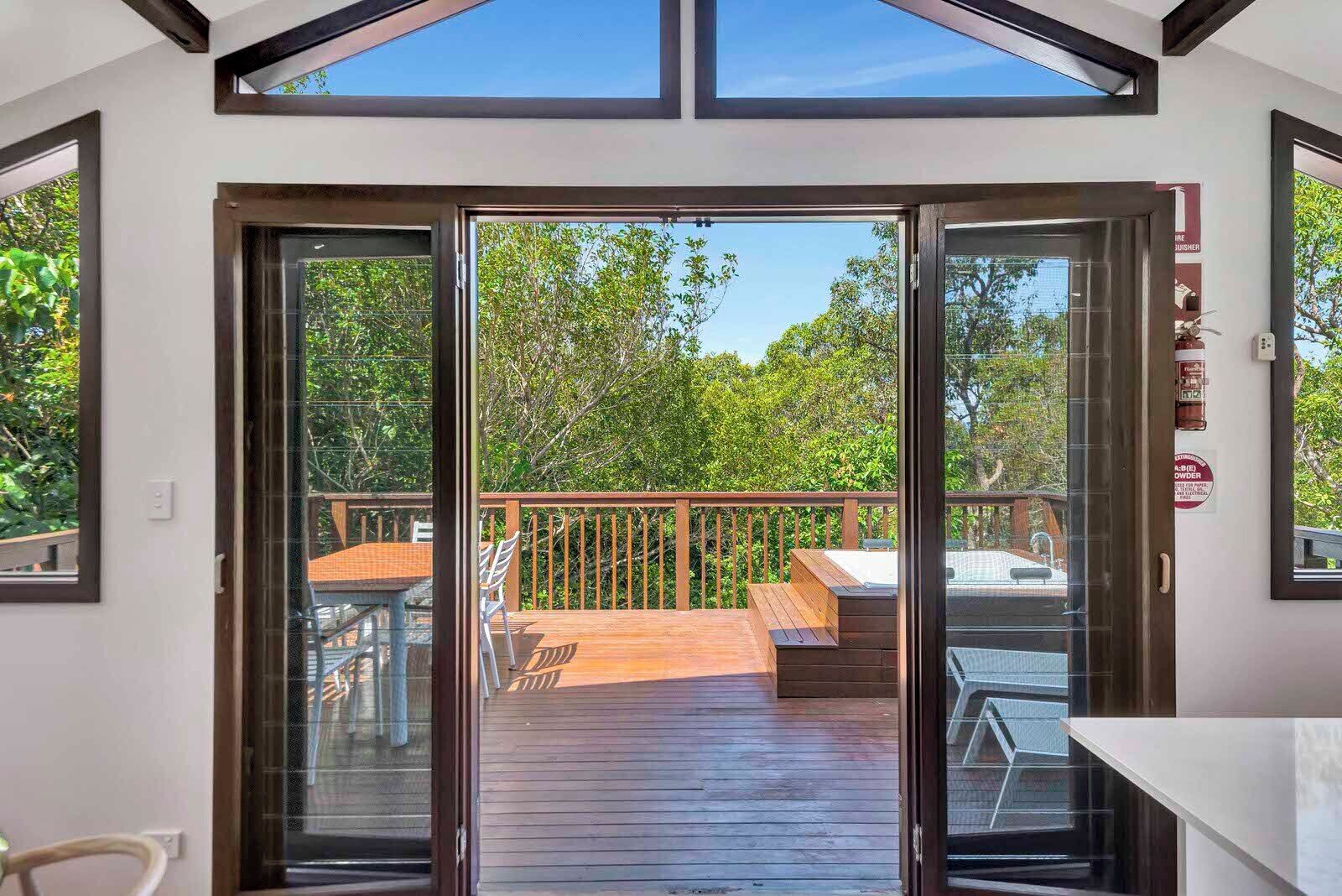 A deck with a wooden floor, a table, and chairs, overlooking a garden with trees.