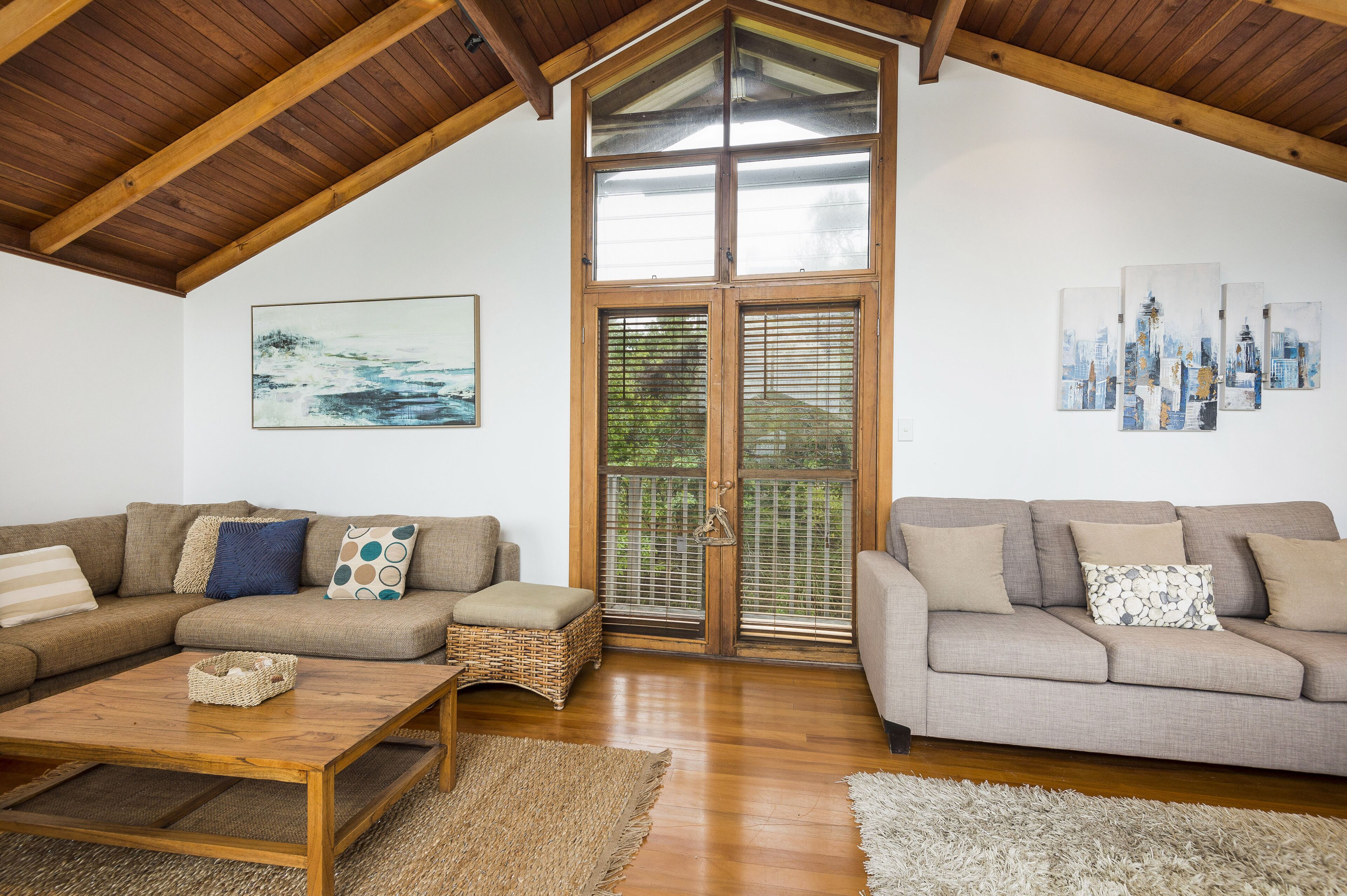 A spacious living room with two sofas, a wooden coffee table, and a large window with blinds.