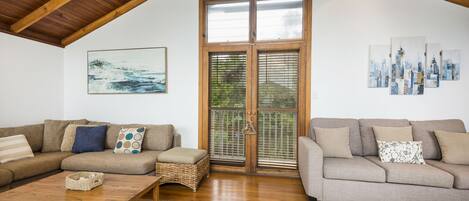 A spacious living room with two sofas, a wooden coffee table, and a large window with blinds.