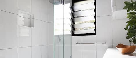 A modern bathroom with white tiles, a glass shower enclosure, and a small window.