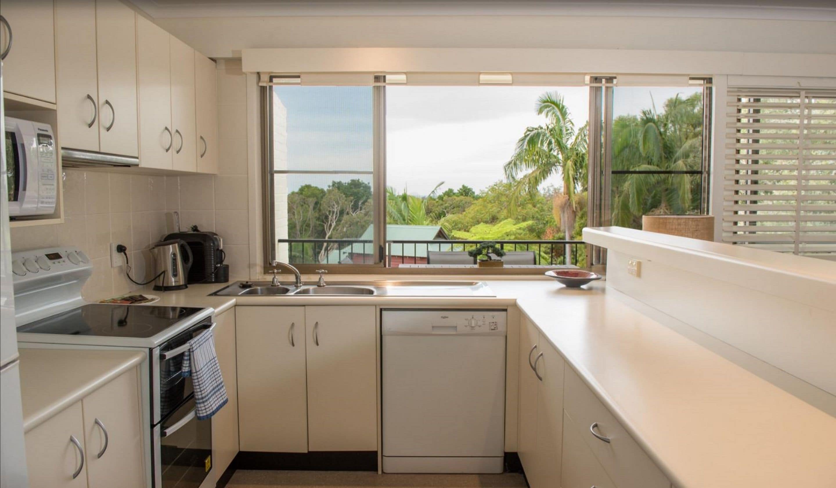 A modern kitchen with a large window, a microwave, a kettle, and a dishwasher.
