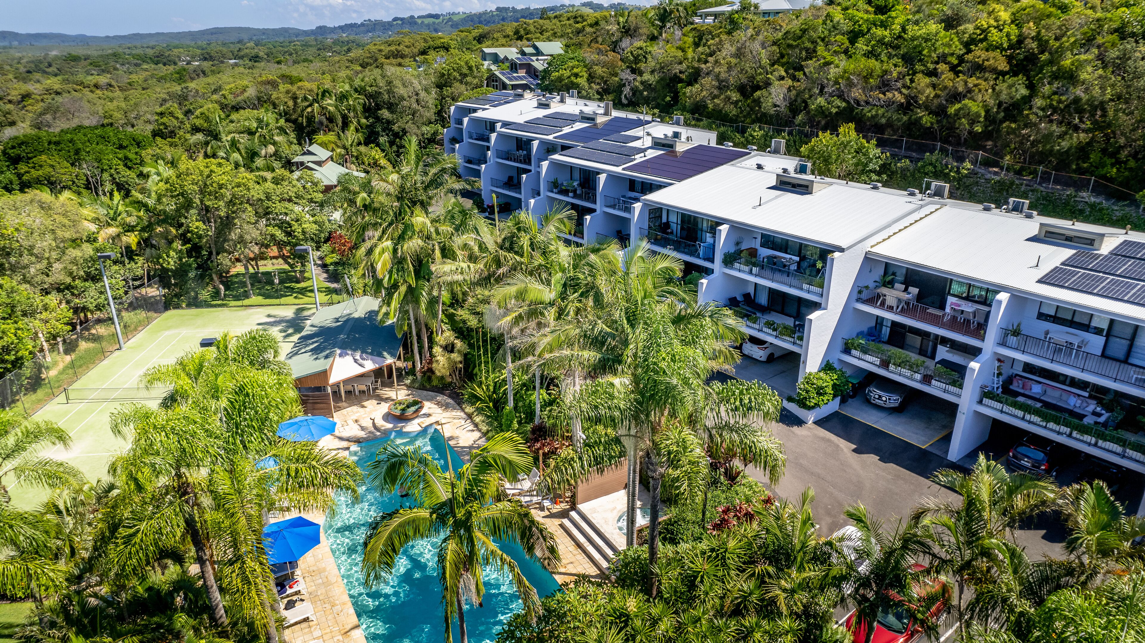 A modern hotel with multiple floors, a rooftop pool, and lush surrounding greenery.
