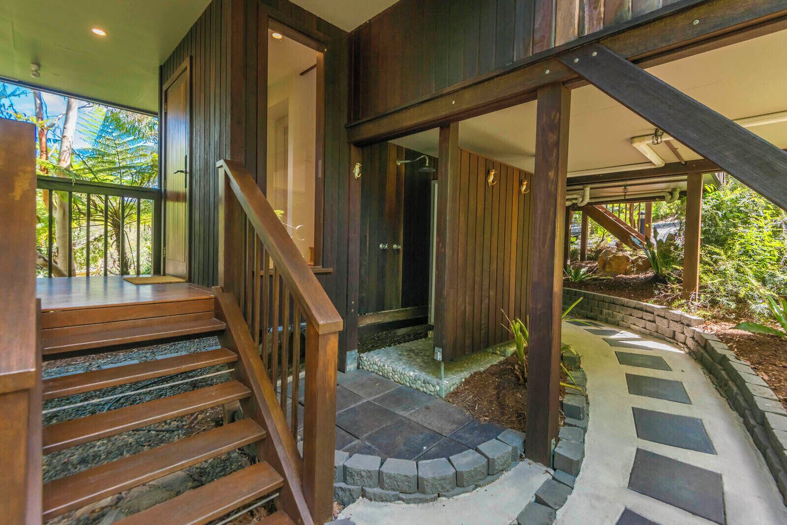 A wooden staircase leading to a glass door, surrounded by a stone pathway and greenery.