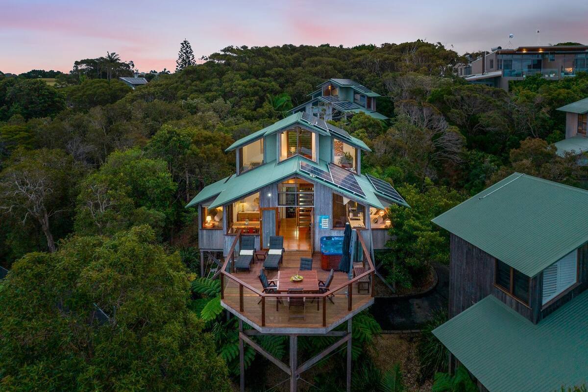 Une maison moderne à plusieurs niveaux, dotée d’une terrasse et entourée d’une forêt dense.
