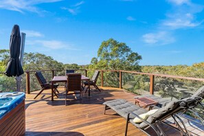 A wooden deck with a table and chairs, a lounge chair, and a hot tub.