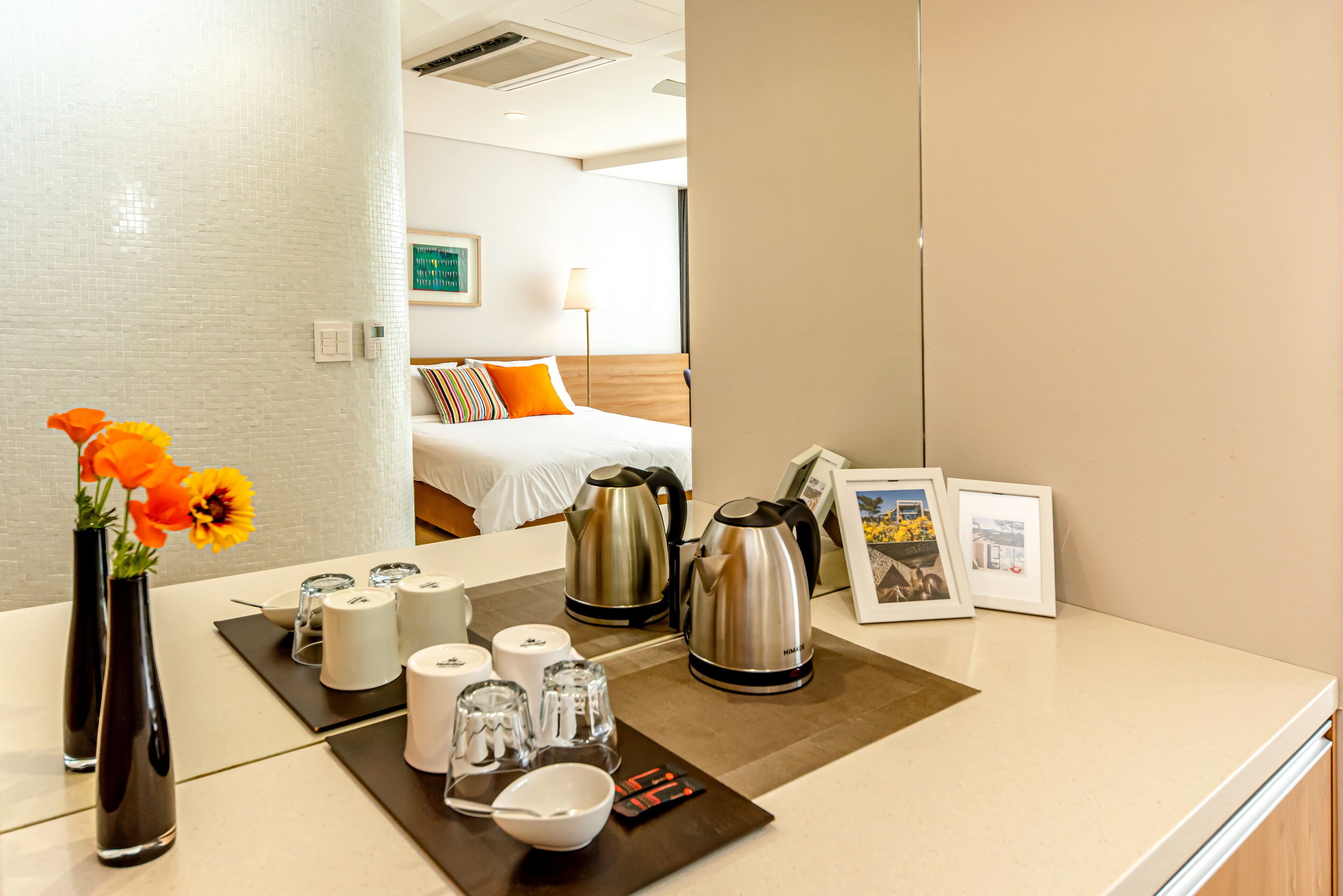 A hotel room with a neatly arranged breakfast table featuring a kettle, cups, and a vase with flowers.
