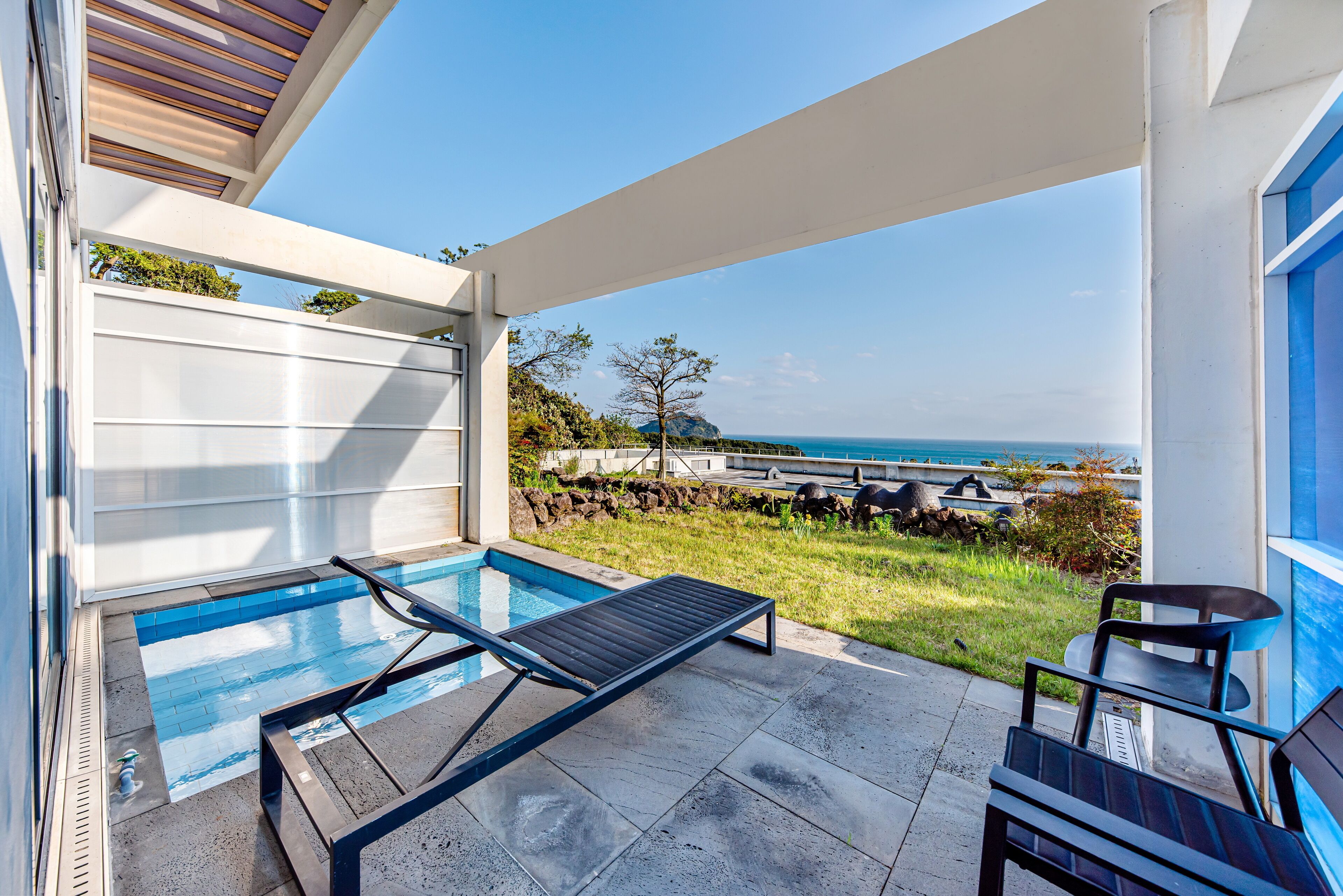A modern outdoor pool area with a view of the ocean, a lounge chair, and a small table.