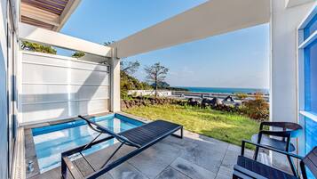 A modern outdoor pool area with a view of the ocean, a lounge chair, and a small table.