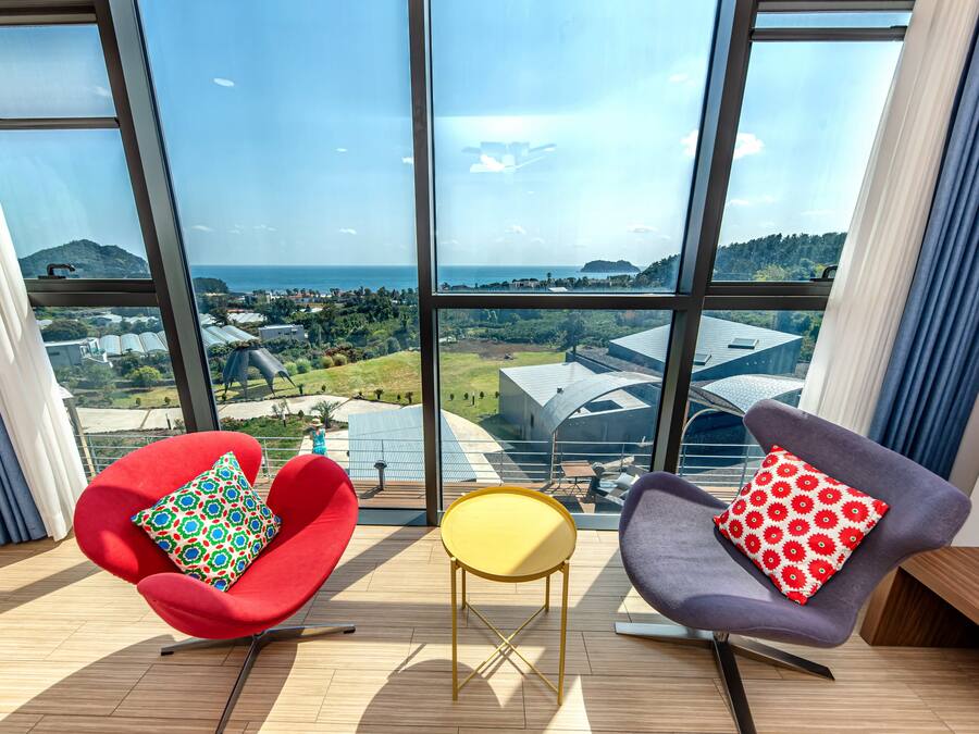 A modern room with large windows, two chairs, a small table, and a view of a coastal landscape.