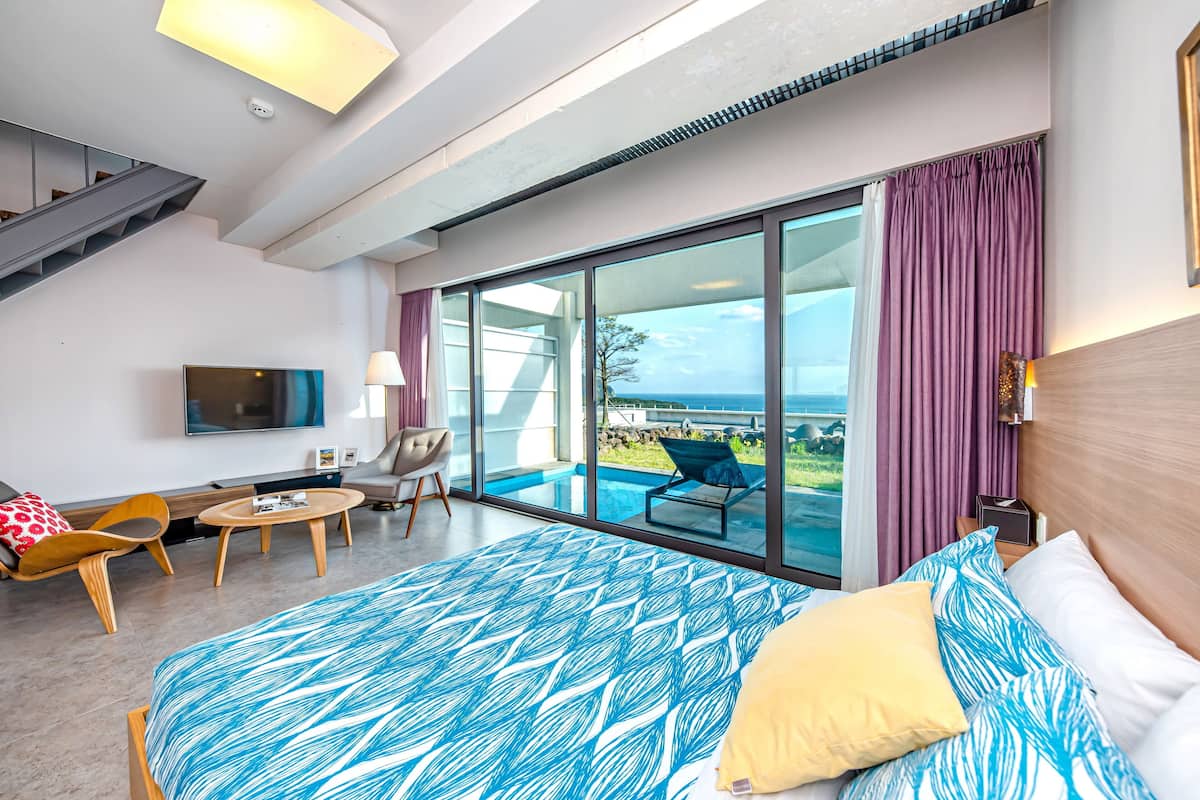 A modern hotel room with a large bed, a TV, a desk, and a balcony with a pool view.