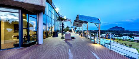 A modern building with large glass windows, a wooden deck, and a view of a distant island.