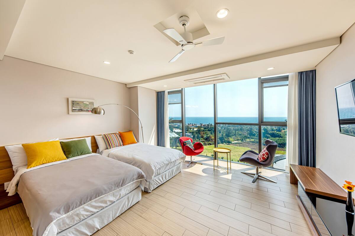 A modern hotel room with a large bed, two chairs, a desk, and a view of the city.