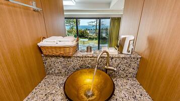 A bathroom with a large, round, amber-colored sink, a wicker basket with towels, and a view of the ocean through large windows.