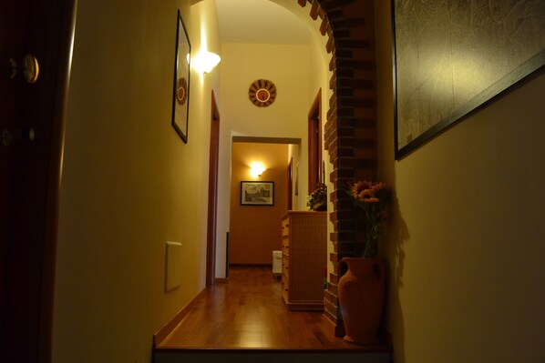 A hallway with wooden flooring, a brick accent wall, a vase with flowers, and a framed picture on the wall. - Enjoy Roma (Rome)