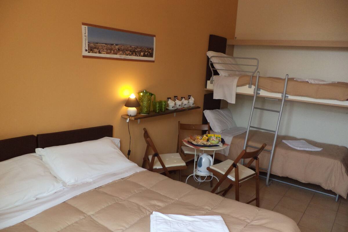 Quarto de hotel com cama, escrivaninha, cadeira, mesa com comida, luminária e quadro na parede.