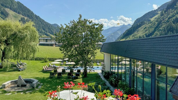 Ein Poolbereich mit Liegestühlen und Sonnenschirmen, umgeben von üppiger Vegetation und Bergen im Hintergrund.