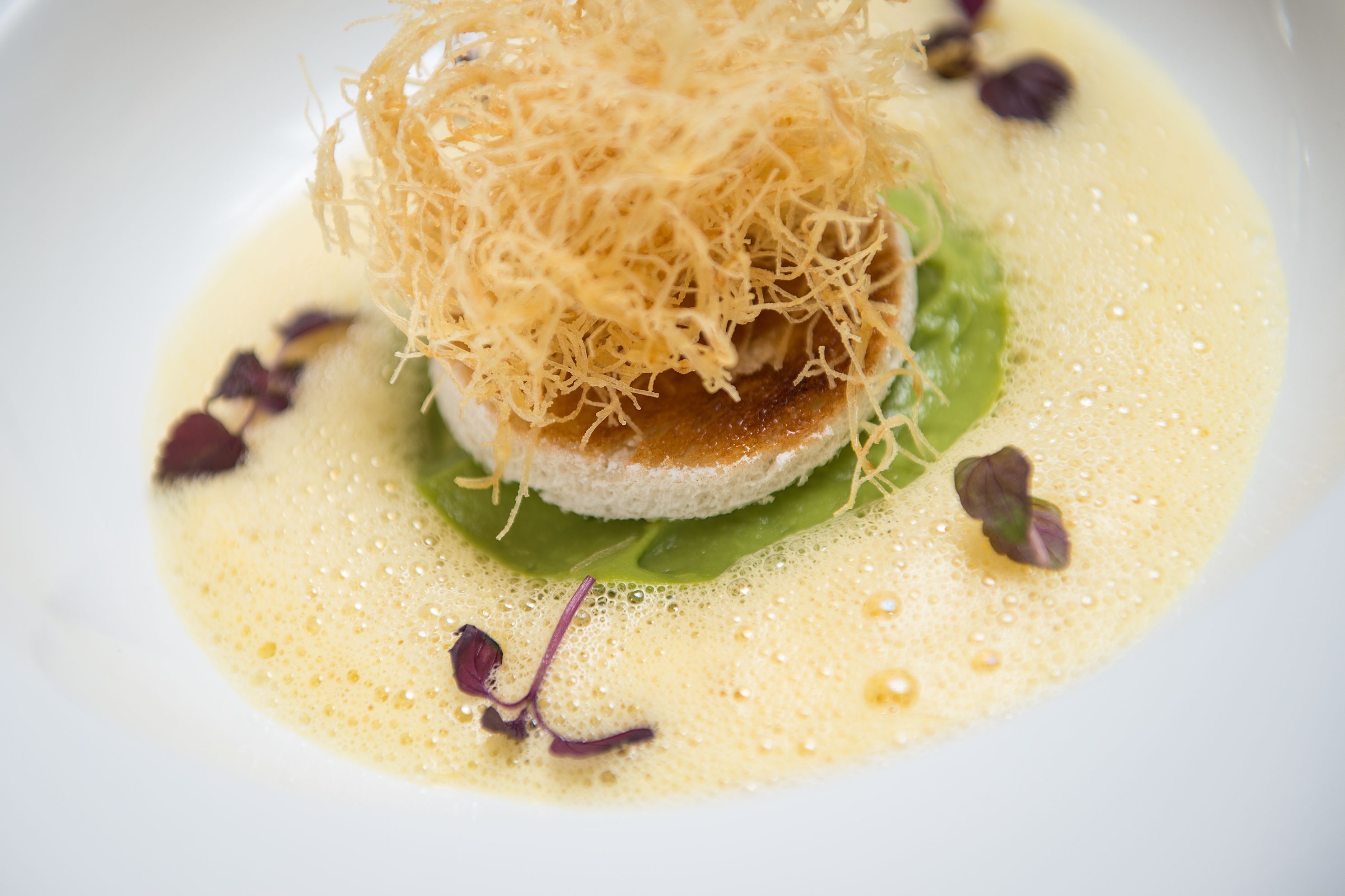 Un plato con cobertura desmenuzada, vegetales de hoja y una salsa.