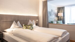 Ein Hotelzimmer mit einem großen Bett, einem Nachttisch, einem Fenster mit Vorhängen und Blick auf Berge.