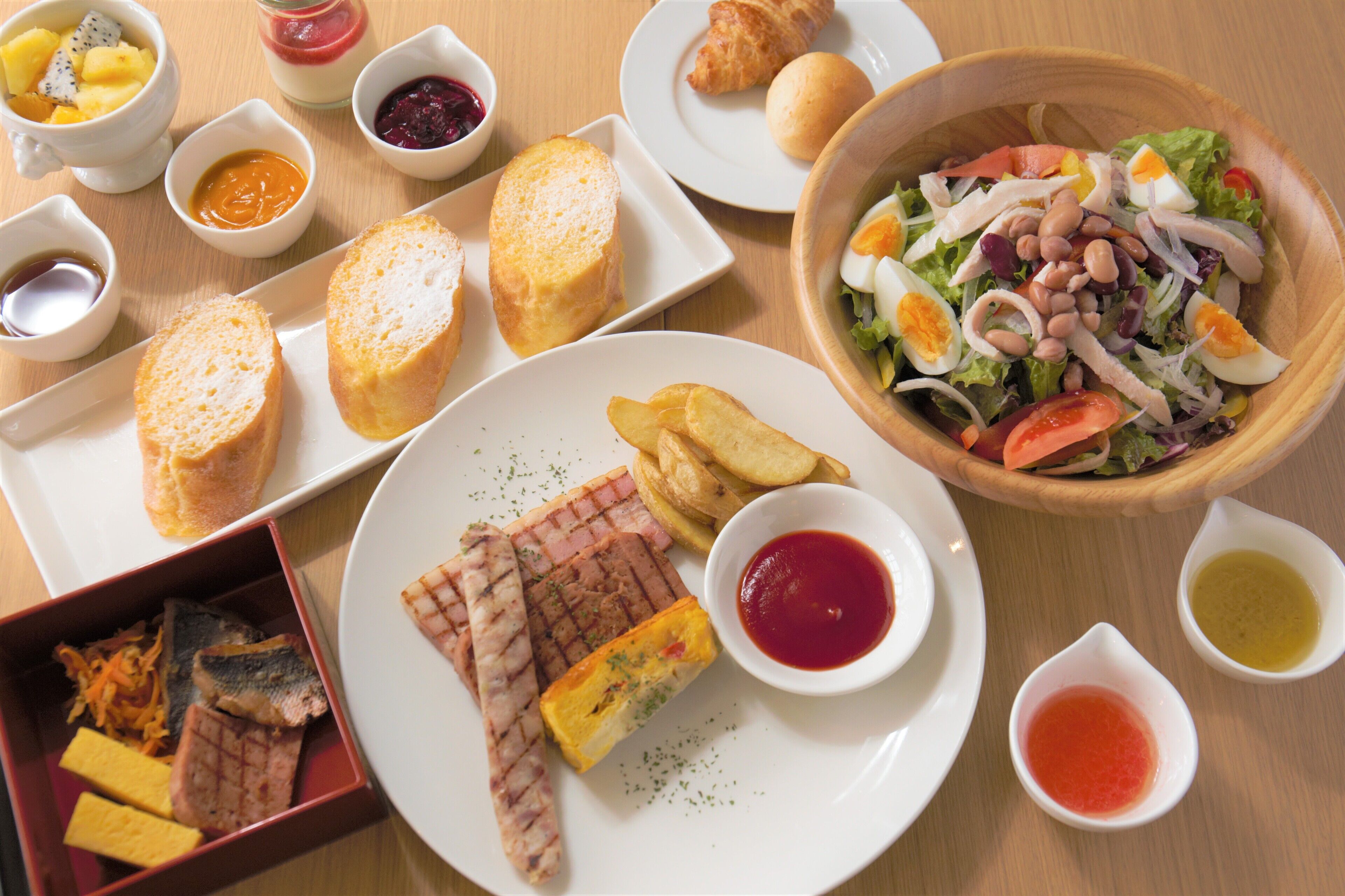 Une variété de plats, notamment une salade, de la viande grillée et du pain, servis sur une table en bois.