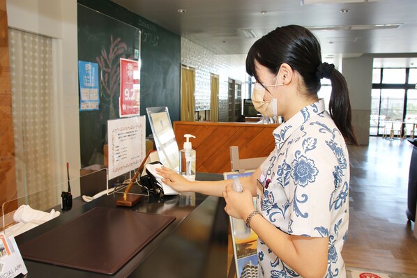 A reception desk with a digital screen, a wooden counter, and a sign with hotel information. - Hotel Sunset Hill (Onna)