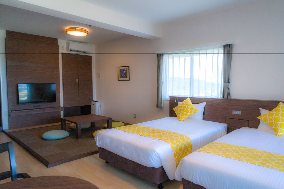 A hotel room with two beds, a TV, a desk, and a window with curtains.